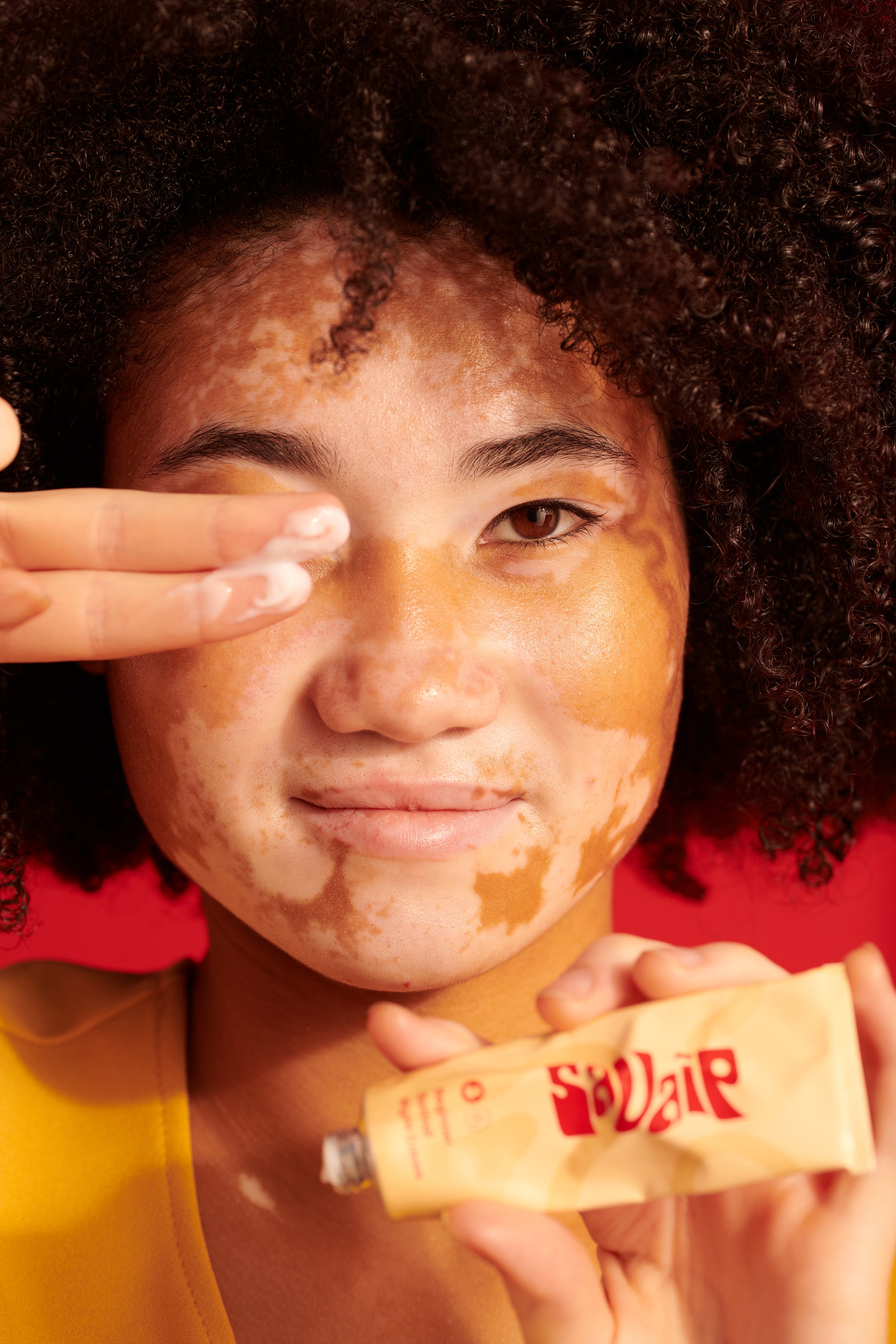 A woman with curly hair applying a product labeled Savaip Beginner Retinol Night cream on her face against a red background.